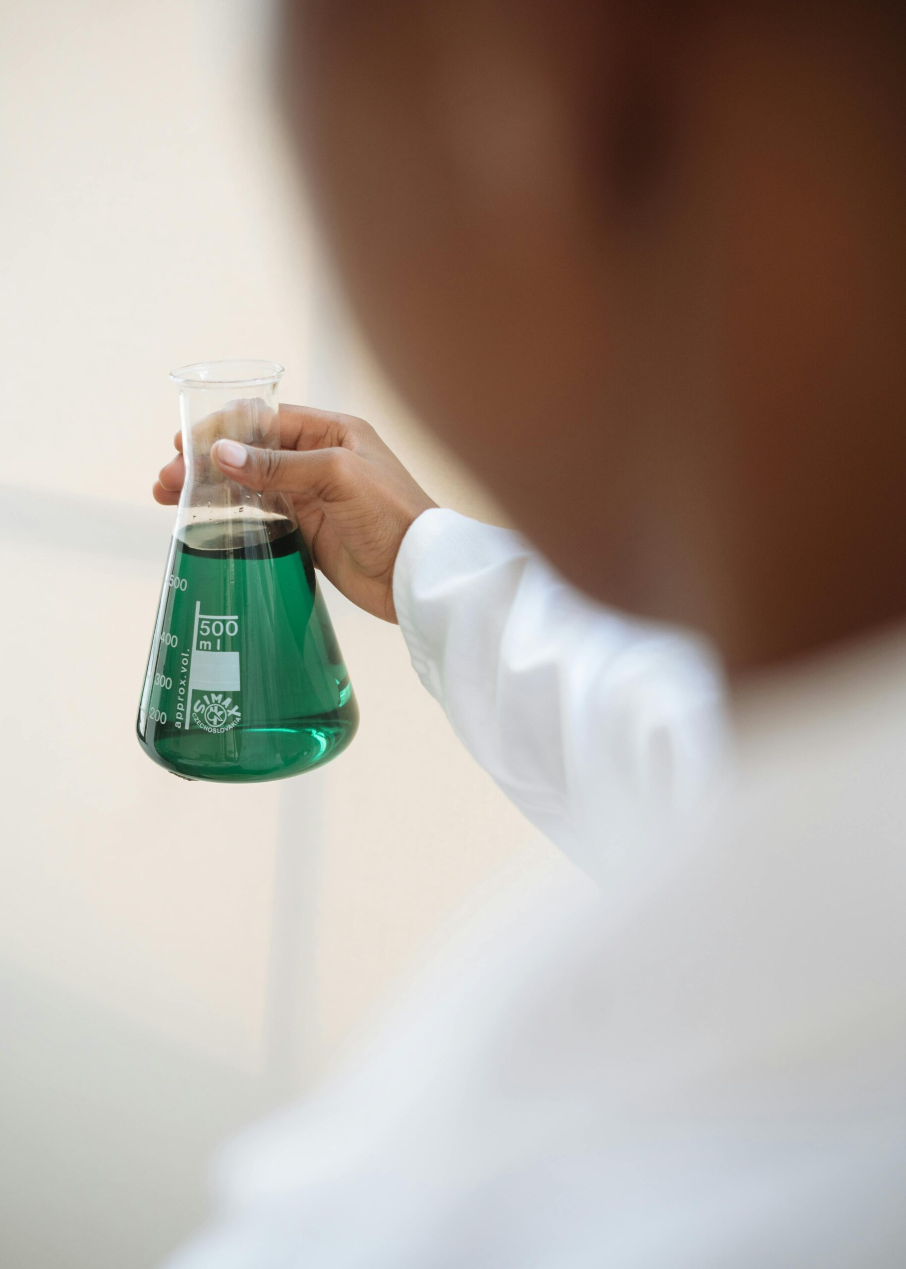 a man holds a beaker filled with a green chemical solution