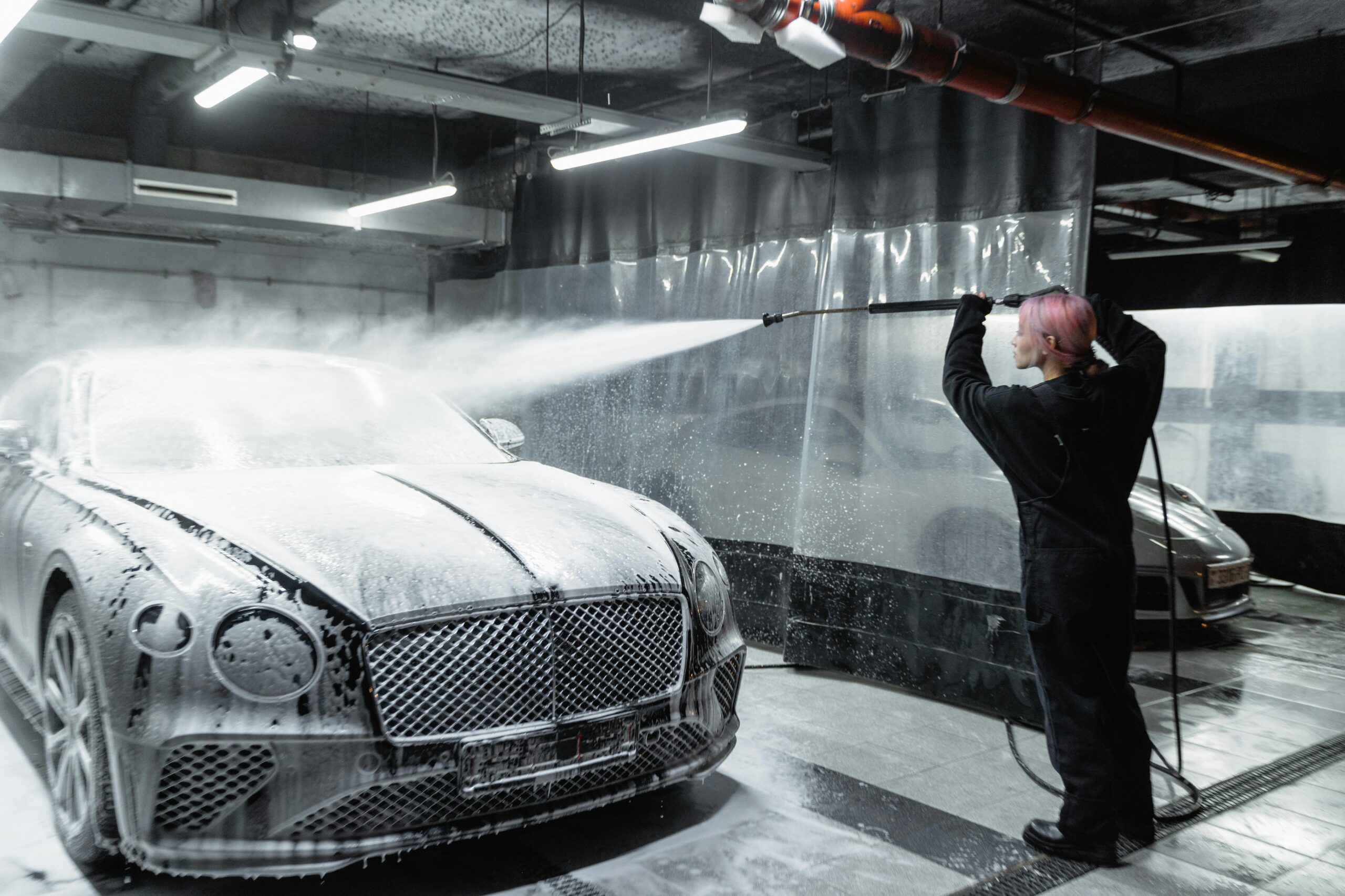 cars stationed in a cleaning bay are cleaned with chemicals and a pressure washer
