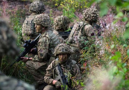 british armed forces crouching in shrubland wearing camoflauge with guns